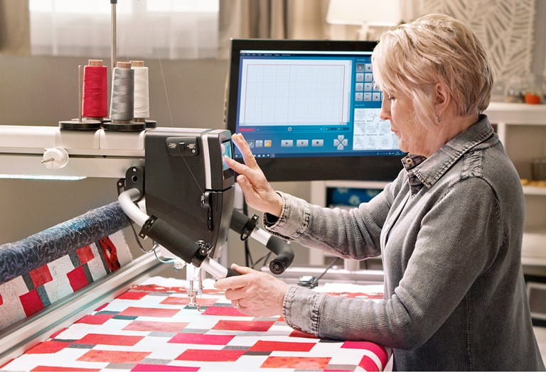 Woman using a longarm with a colorful quilt